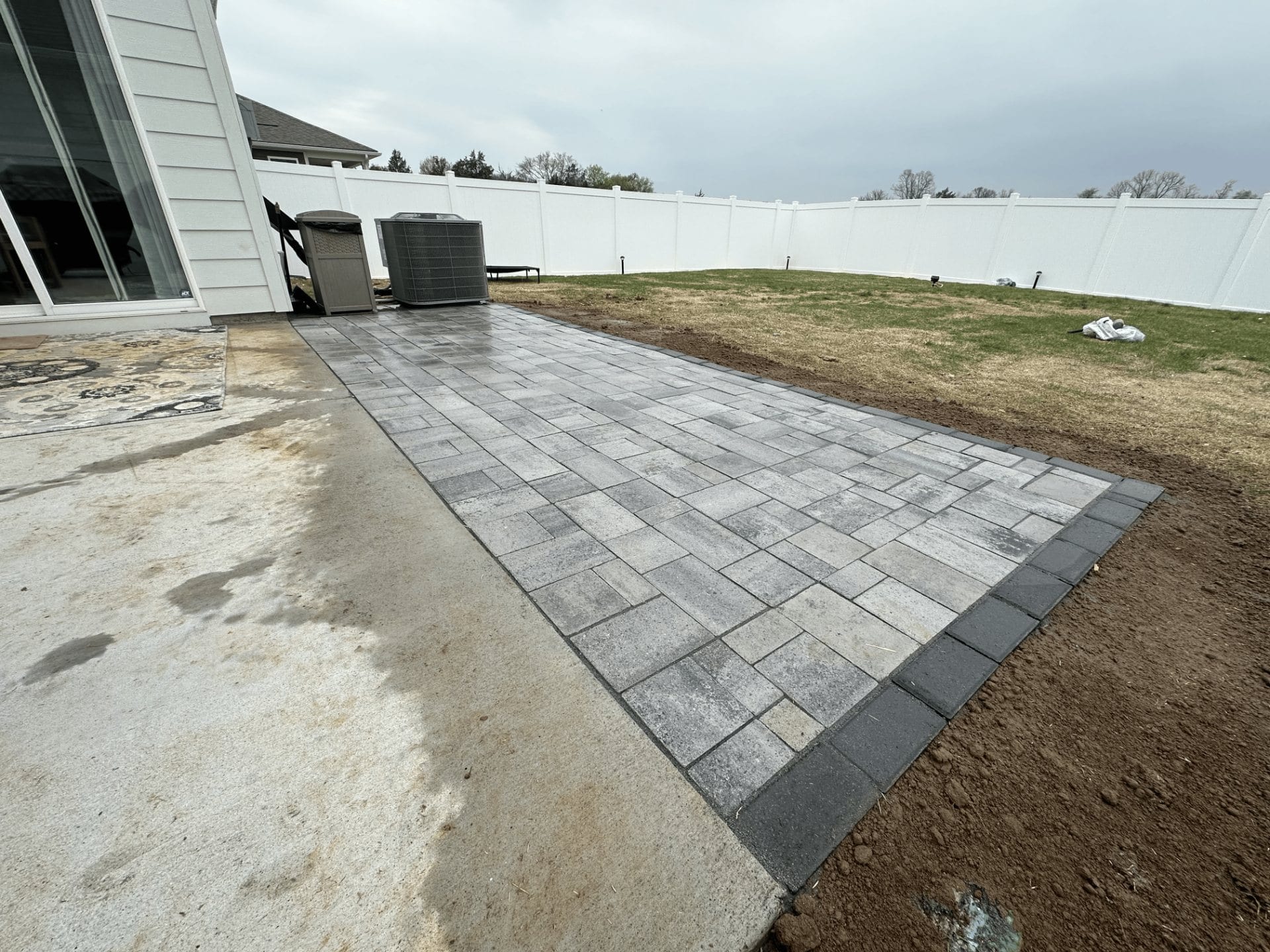 Grey paver patio with charcoal border along a home