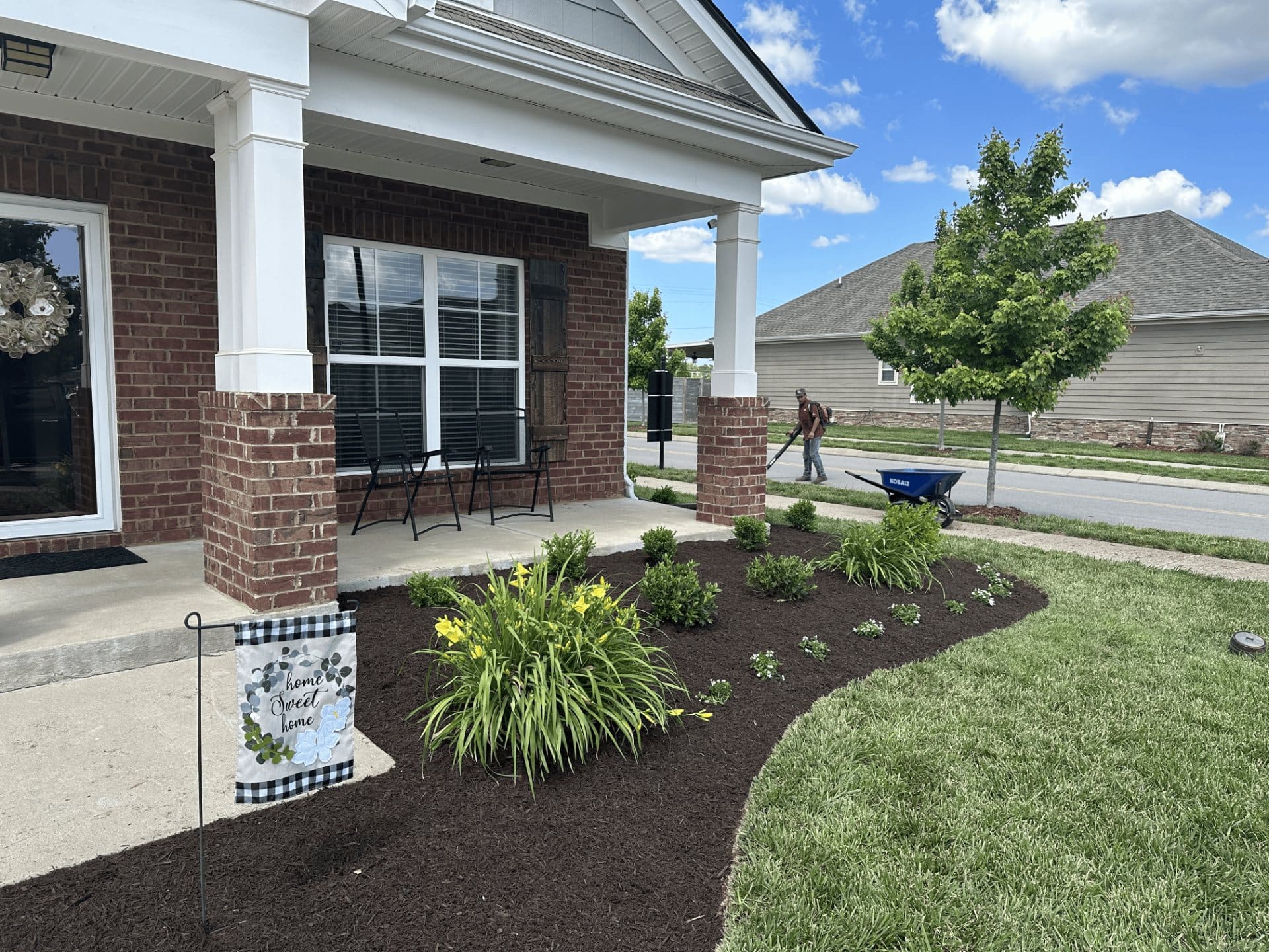 Fresh mulch bed with daylilies and shrubs along a brick porch